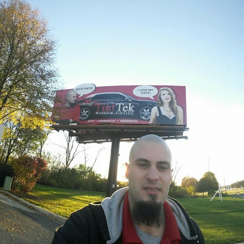 Jeremy Ryan in front of a Tint Tek window-tinting billboard at dusk.